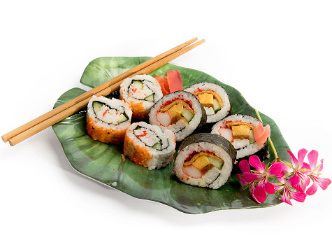 Banana leaf-shaped dish of crab and cucumber sushi with chopsticks and flower garnish.