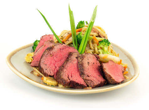 Sliced medium-rare steak on a plate with sauteed vegetables.