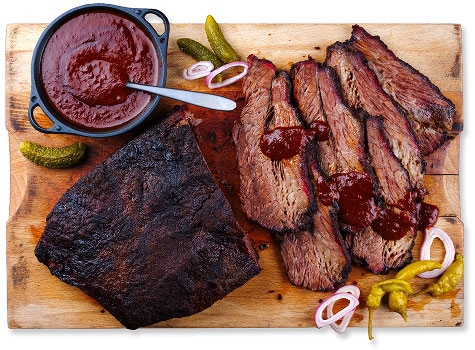 Platter of smoked and sliced brisket with pickles and onions, and a bowl of barbecue sauce.