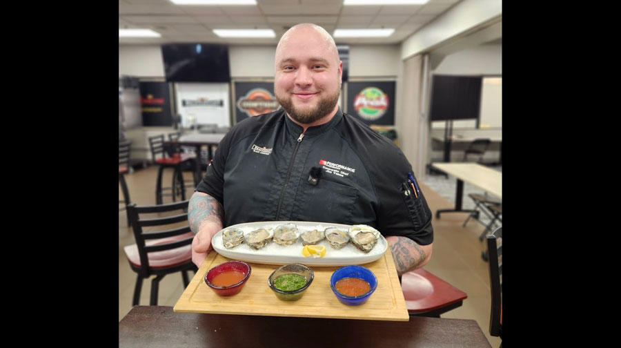 Chef holding a tray of cold oysters on the half shell on ice, with a variety of sauces.