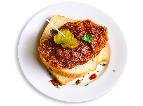 Nashville hot breaded chicken on slices of white bread, slathered in sauce and with a pickle on a toothpick.
